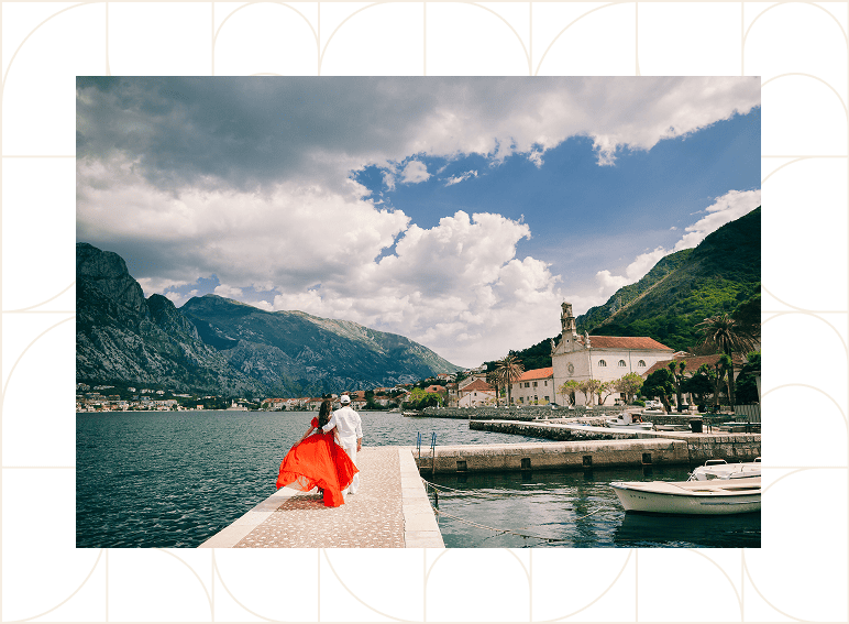 A couple strolls along a dock with a mountain backdrop, enjoying a scenic view together.