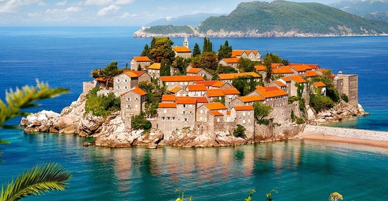 Sveti Stefan, a small island with buildings and trees surrounded by water, under a clear sky.