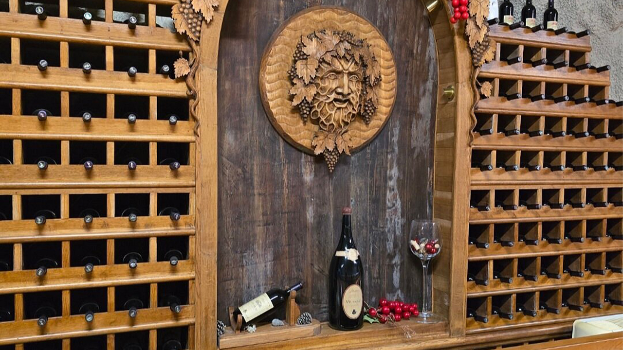 Wooden wine rack with bottles and a carved grape motif centerpiece at Plantaže winery.